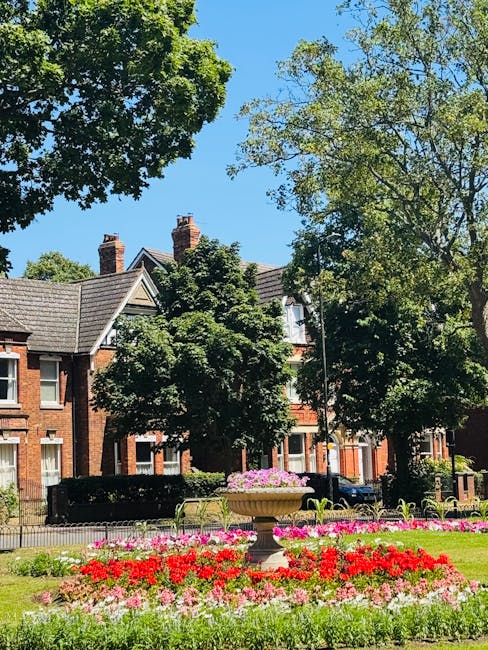 A landscaped garden area featuring a wide gravel pathway bordered by a well-maintained lawn with a few decorative orange spheres and black metal benches. To the right, a set of stone steps bordered by